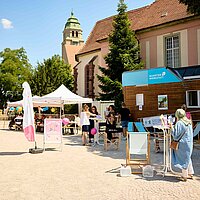 Ein Platz mit einem Tiny House, Sonnenschirmen und Menschen, die sich unterhalten