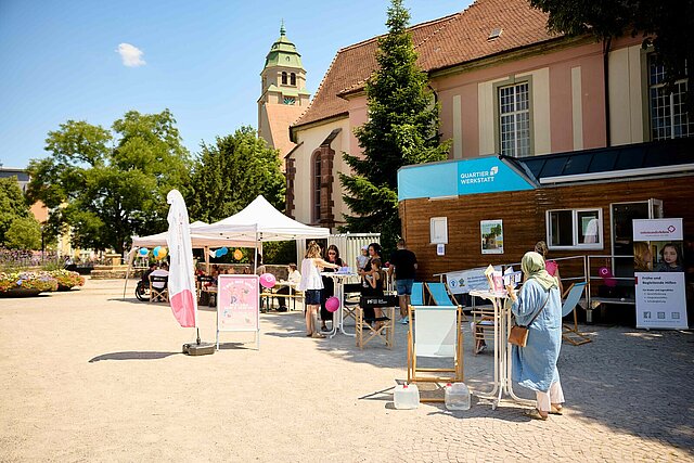 Ein Platz mit einem Tiny House, Sonnenschirmen und Menschen, die sich unterhalten