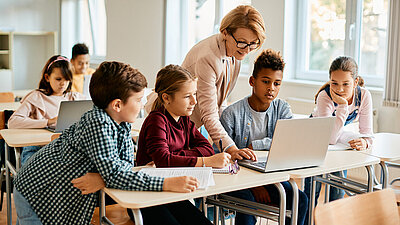 Eine Gruppe von Grundschülern hat mit ihrer Lehrerin im Klassenzimmer Computerunterricht.