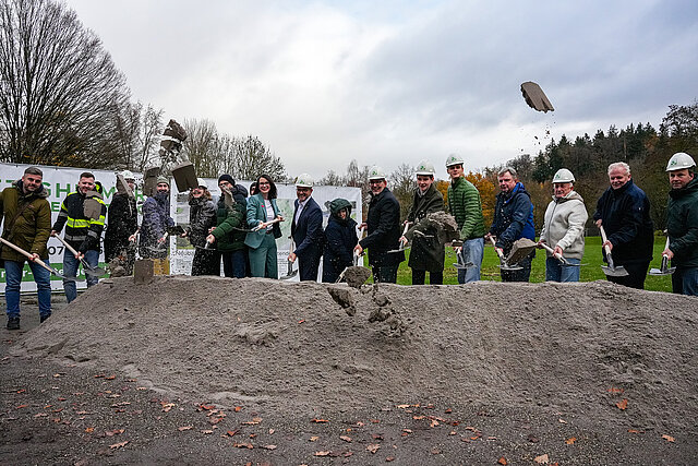 Auf dem Bild sind viele, darunter auch Oberbürgermeister Peter Boch zu sehen, die mit Schaufeln Sand in die Luft werden als symbolischer Spatenstich für den Skatepark im Enzauenpark.