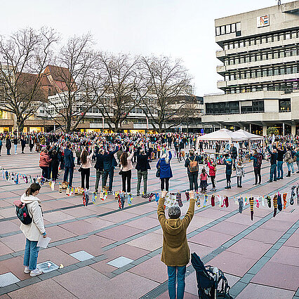 Viele Menschen halten gemeinsam eine lange Leine nach oben, auf der bunte Socken hängen - copyright:Indigo Pictures