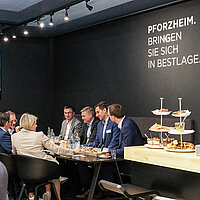 Farbfoto: Menschengruppe sitzt am Tisch auf dem Pforzheimer Messestand