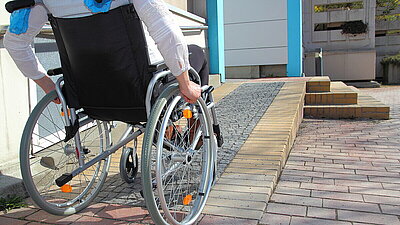 Mensch im Rollstuhl fährt eine Rampe hoch: Barrierefreies Gebäude.