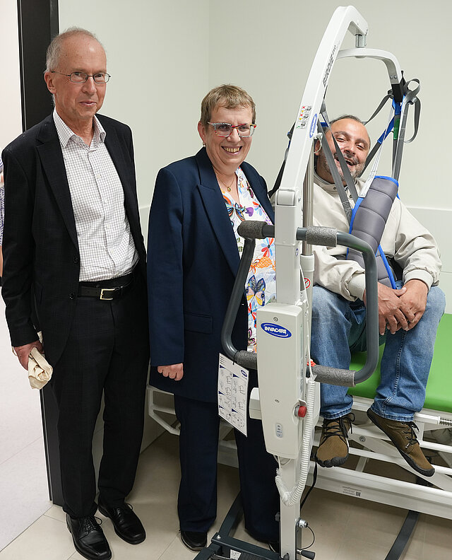 Drei Personen, eine in einer Hebevorrichtung, die die Toilette für alle im neuen Technischen Rathaus vorführen. 