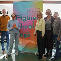 Fünf Personen vor einem Roll-Up mit der Aufschrift "Figurentheatertage" 