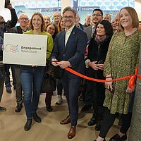 Ein Mann schneidet ein rotes Band durch, hinter ihm stehen mehrere Menschen