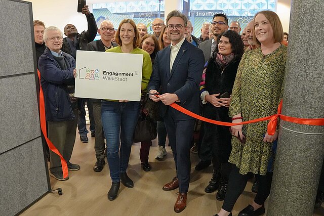 Ein Mann schneidet ein rotes Band durch, hinter ihm stehen mehrere Menschen