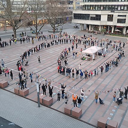 Viele Menschen halten gemeinsam eine lange, spiralförmig angerichtete Leine nach oben, auf der bunte Socken hängen. Das Foto ist von oben aufgenommen. - copyright:Stadt Pforzheim