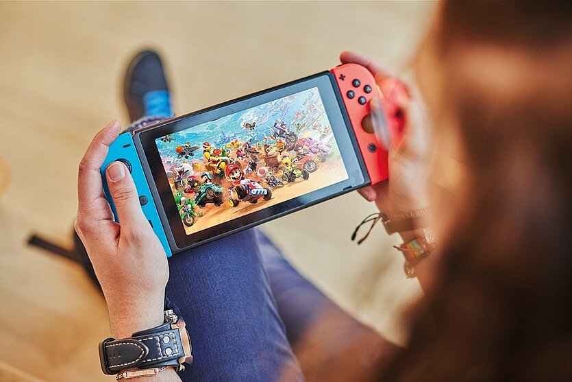 Fotografie: die Konsole Nintendo Switch wird in zwei Händen gehalten. Es wird darauf ein Rennspiel gespielt.  - copyright: Stadtbibliothek Pforzheim - Ersteller: Daniel Foltin
