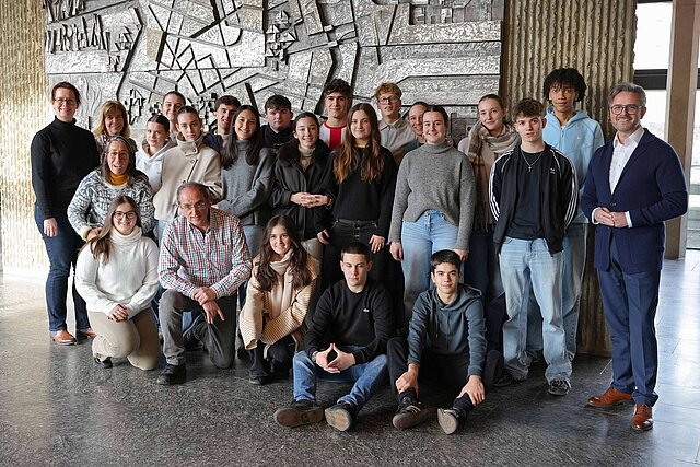 Viele Menschen vor einer grauen Steinwand. 