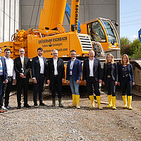Farbfoto: Gruppenbild auf einer Baustelle vor einem orangefarbenen Kran.