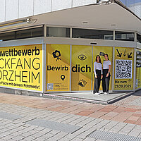 Zwei Frauen stehen vor einem mit gelber Folie beklebten Schaufenster mit der Aufschrift "Ideenwettbewerb Blickfang Pforzheim"