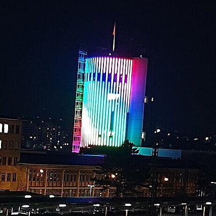 Auf dem Foto sieht man den Sparkassenturm Pforzheim. Der Sparkassenturm ist bunt in den Farben Lila, blau, grün, gelb, rot, orange, rosa beleuchtet. Die Farben sind diagonal angeordnet. Das Foto wurde im Dunkeln aufgenommen. - copyright:Stadt Pforzheim