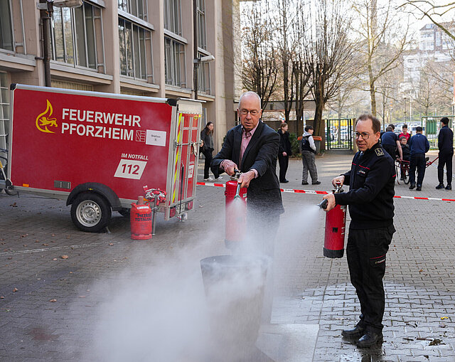Schulbürgermeister Frank Fillbrunn (links) und Feuerwehrkommandant Sebastian Fischer löschen mit zwei Feuerlöschern ein Übungsfeuer beim Aktionstag.