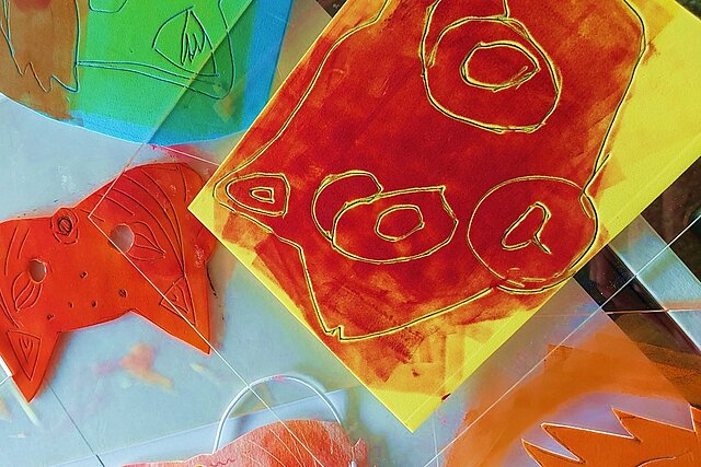 Bunte Tiermasken aus Papier in verschiedenen Farben, darunter rote, orange und grüne Masken, die in einem Druckworkshop erstellt wurden. - copyright:Stadt Pforzheim