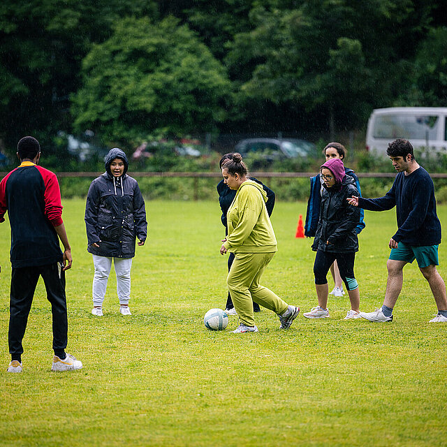 Es sind zwei Männer und fünf Frauen zu sehen. Eine Frau im grünen Jogginganzug spielt den Ball. - copyright:Stadt Pforzheim