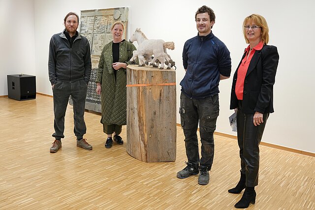 Vier Personen neben einer Holz-Skulptur eines Pferdes.
