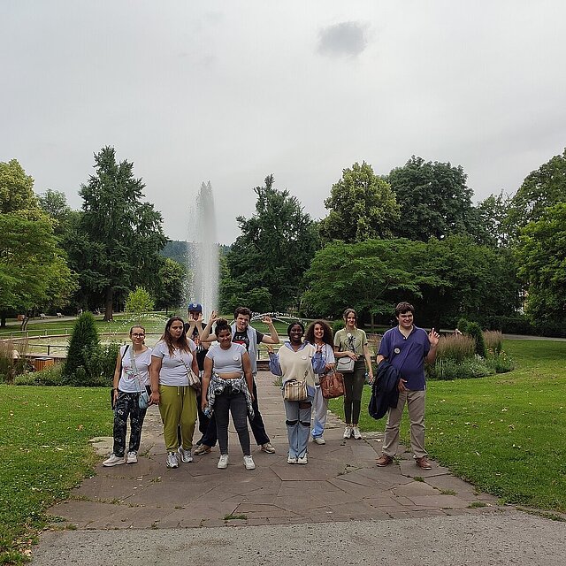 Neun junge Frauen und Männer stehen vor einem Brunnen im Stadtpark Pforzheim.  - copyright:Stadt Pforzheim