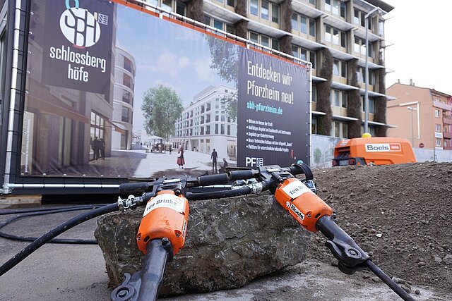 Foto: Presslufthammer im Vordergrund, Hintergrund: Plakat des Bauprojekts "Schlossberghöfe" (SBH) - copyright:Stadt Pforzheim