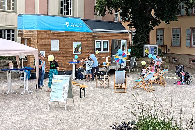 Ein Tiny House steht auf einem Platz, davor sind Kinder und Erwachsene zu sehen.