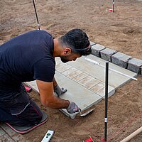Farbfoto: Mann verlegt Bodenplatten im abgezäunten Bereich