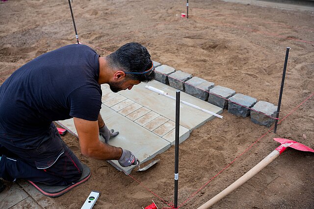 Farbfoto: Mann verlegt Bodenplatten im abgezäunten Bereich
