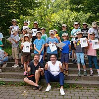 Bürgermeister Tobias Volle und Tierpfleger David Schmitt freuen sich gemeinsam mit 23 frisch gebackenen Junior-Rangerinnen und -Rangern über die bestandene Ausbildung.