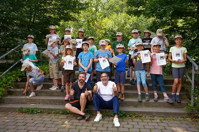 Bürgermeister Tobias Volle und Tierpfleger David Schmitt freuen sich gemeinsam mit 23 frisch gebackenen Junior-Rangerinnen und -Rangern über die bestandene Ausbildung.