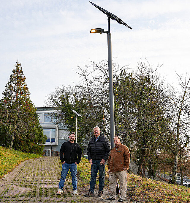 Marco Schäfer, Sachgebietsleitung Gebäudeunterhaltung im Gebäudemanagement, Uwe Weiss, Abteilungsleiter Straßenneubau und Verkehrstechnik im Grünflächen- und Tiefbauamt sowie Michael Disch, Straßenneubau und Verkehrstechnik im Grünflächen- und Tiefbauamt (von links) stehen vor einer der neuen Straßenlampen, die mit Solarstrom betrieben werden.