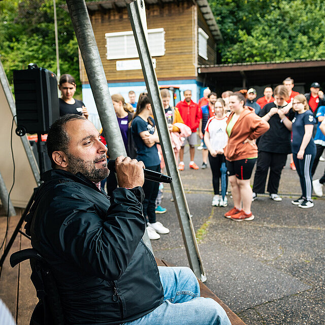 Ein Mann im Rollstuhl steht auf einer Bühne und spricht durch ein Mikrophon. - copyright:Stadt Pforzheim