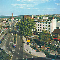 Farbfoto von 1970: Mehrspurige Straße am Bahnhofplatz. Im Hintergrund die St.-Franziskus-Kirche. - copyright:Fotoverlag Günter Beck